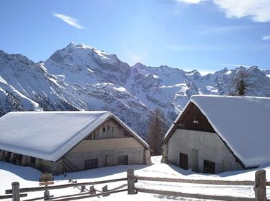 Two snow-covered mountain huts with a stunning Alpine backdrop under bright winter sun.