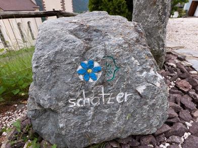 Grande pietra grigia con un fiore blu dipinto e la scritta “schatzer”